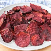 air fried beet chips on white plate with wood underneath