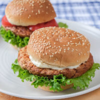 two turkey burgers with buns on white plate on wooden board
