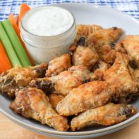 chicken wings in bowl with dipping sauce and cut veggies behind