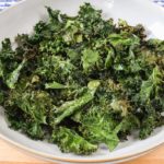bowl full of green kale chips on wooden board