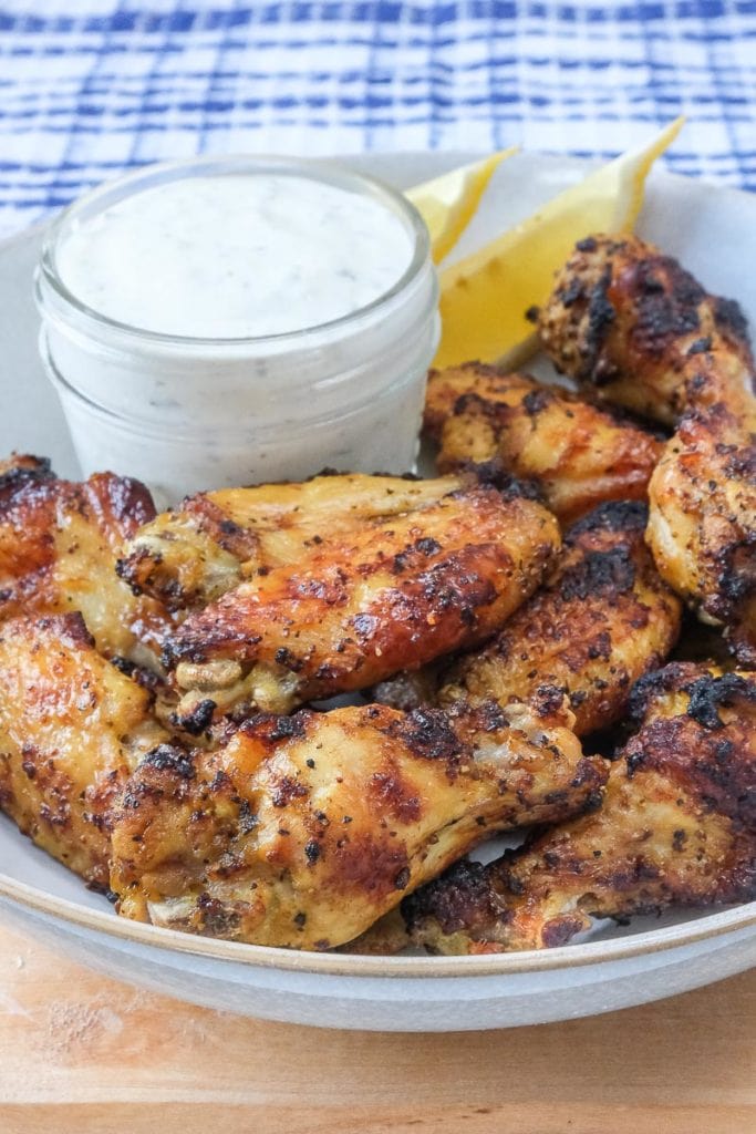 lemon pepper chicken wings in bowl on wooden board with sauce behind