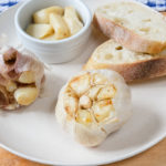 bulb of roasted garlic on plate with bread behind