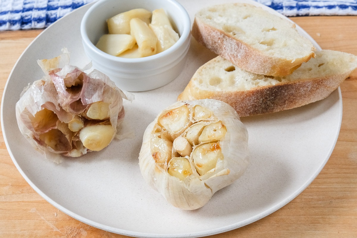 bulb of roasted garlic on plate with bread behind
