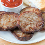 cooked sausage patties on white plate with ketchup behind