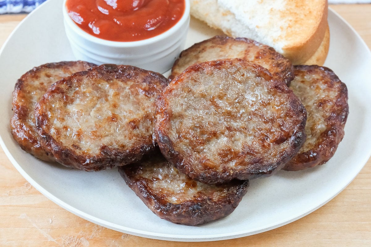 cooked sausage patties on white plate with ketchup behind