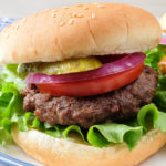 Photo of hamburger on bun with lettuce, tomato, onion and pickle on blue plate and text overlay saying "air fryer juicy hamburger"