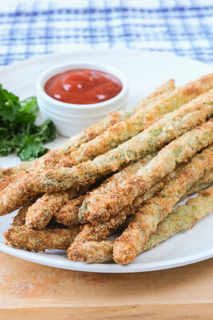 breaded asparagus fries on white plate with ketchup behind