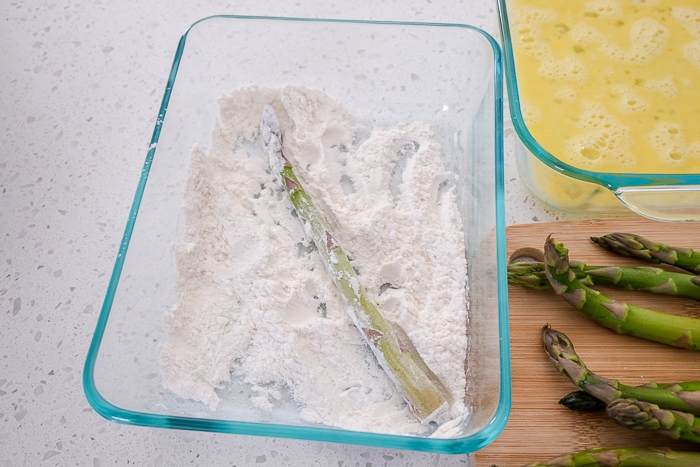 asparagus stalk in container of flour on white counter