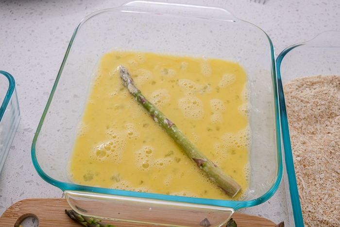 asparagus stalk in container of beaten egg on countertop