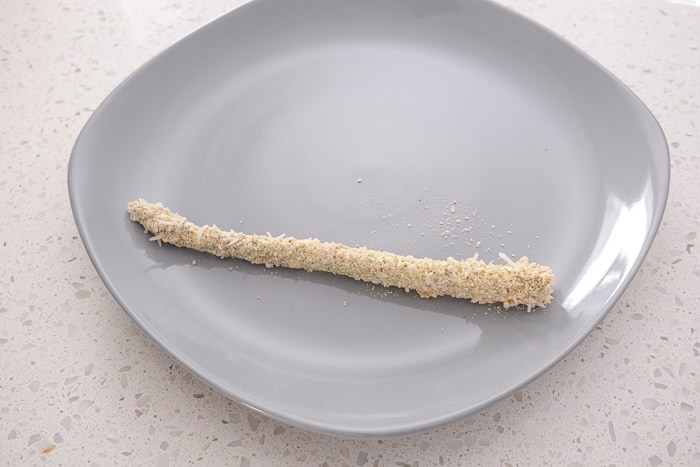 one stalk of breaded asparagus on grey plate on counter
