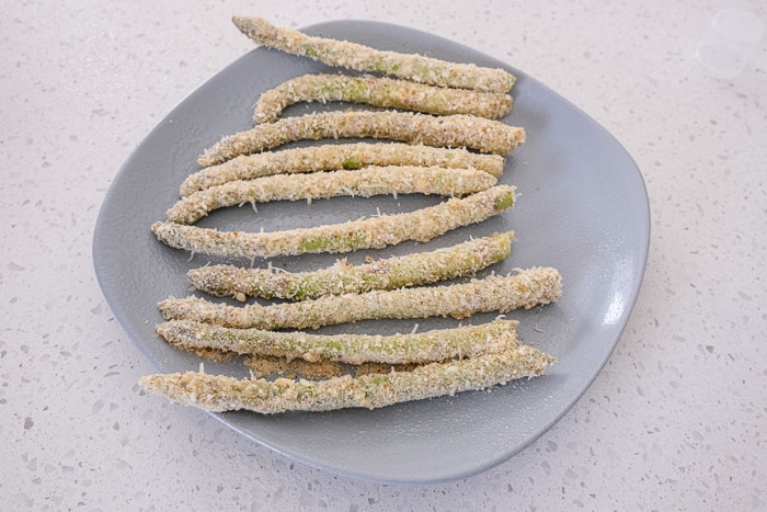 many stalks of breaded asparagus on grey plate on counter