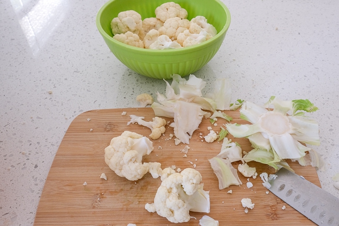 cutting cauliflower florets on wooden board with green bowl behind
