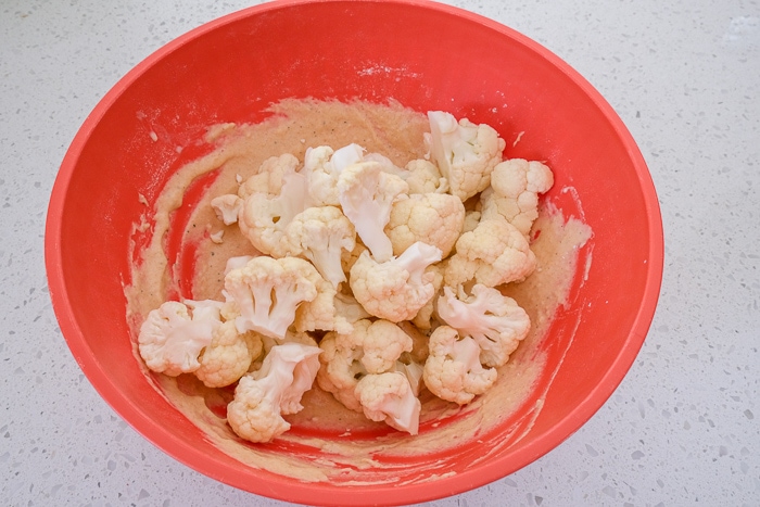 raw cauliflower florets in red bowl of batter on white counter