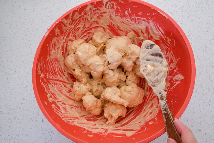 wooden spoon mixing cauliflower florets in batter in red plastic bowl