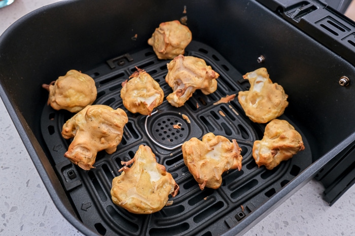 cooked battered cauliflower bites in black air fryer tray on white counter