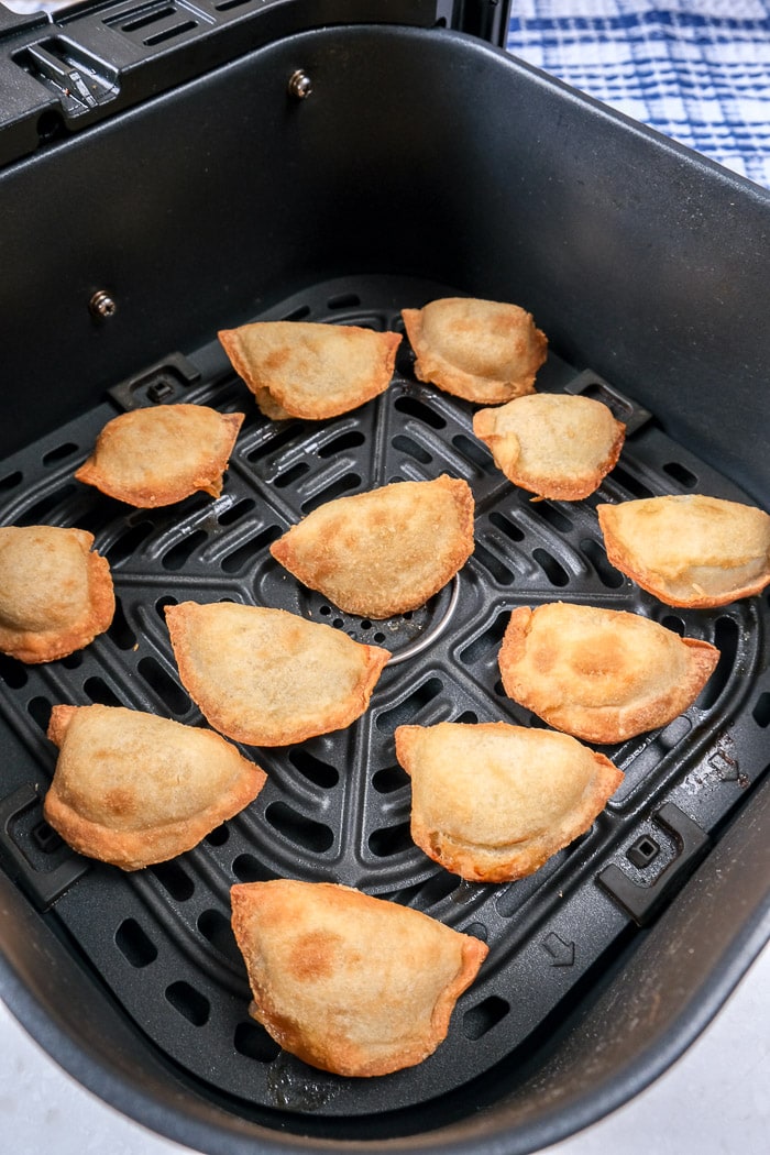 cooked mini empanadas in black air fryer tray on counter