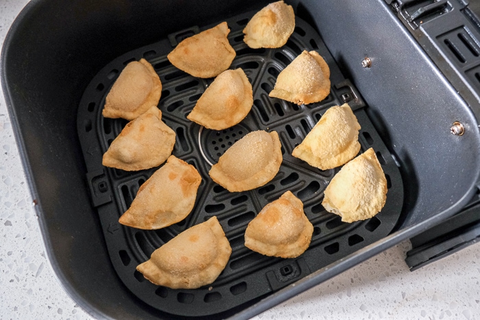 frozen mini empanadas in black air fryer tray on white counter
