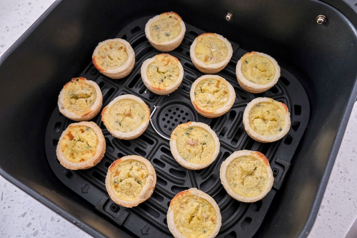frozen mini quiche in black air fryer tray on counter