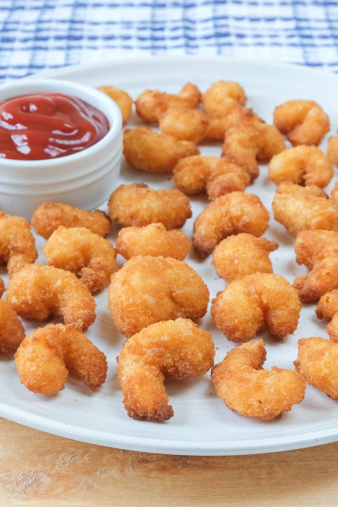 breaded popcorn shrimp on plate on wooden board with ketchup behind