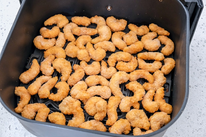 frozen popcorn shrimp in black air fryer tray on counter top