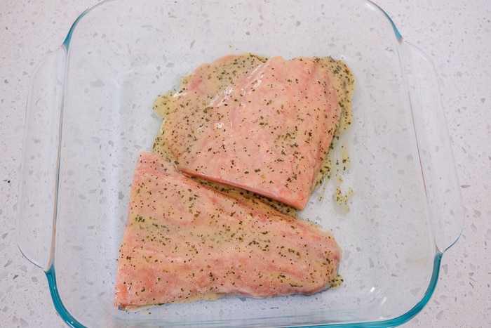 frozen salmon fillets in clear glass dish with marinade on top