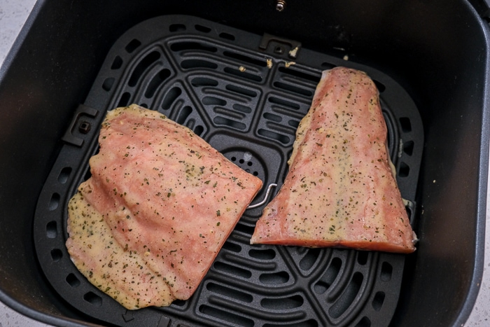 uncooked salmon fillets covered in spices laying in black air fryer tray