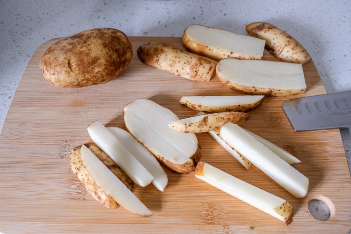 russet potatoes cut into fries on wooden cutting board
