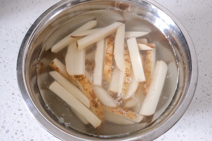 cut fries soaking in silver bowl of water on white counter