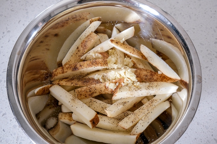 raw fries in silver bowl with spices on top on white counter