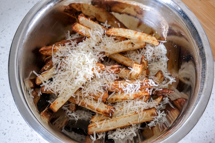 fresh cooked fries in silver bowl covered in shredded parmesan cheese on counter