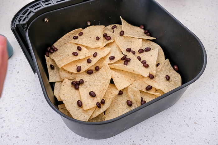 tortilla chips in black air fryer tray with black beans on top