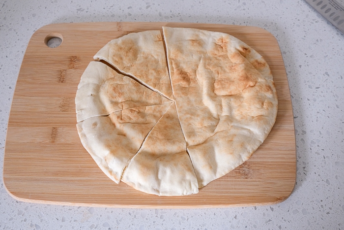 round pita cut into triangles on wooden cutting board on white counter