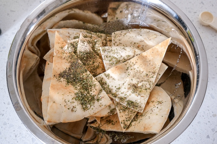 pita triangles in silver mixing bowl covered in oil and spices