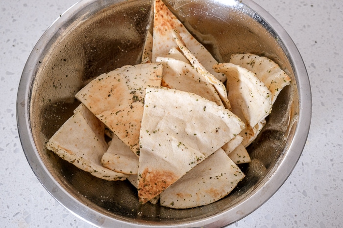 pita triangles in silver bowl on counter with oil and spices