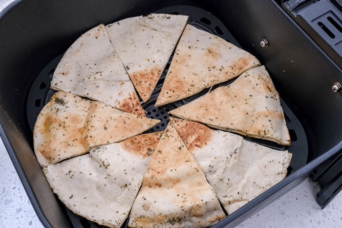 pita triangles covered in spices in black air fryer tray on white counter