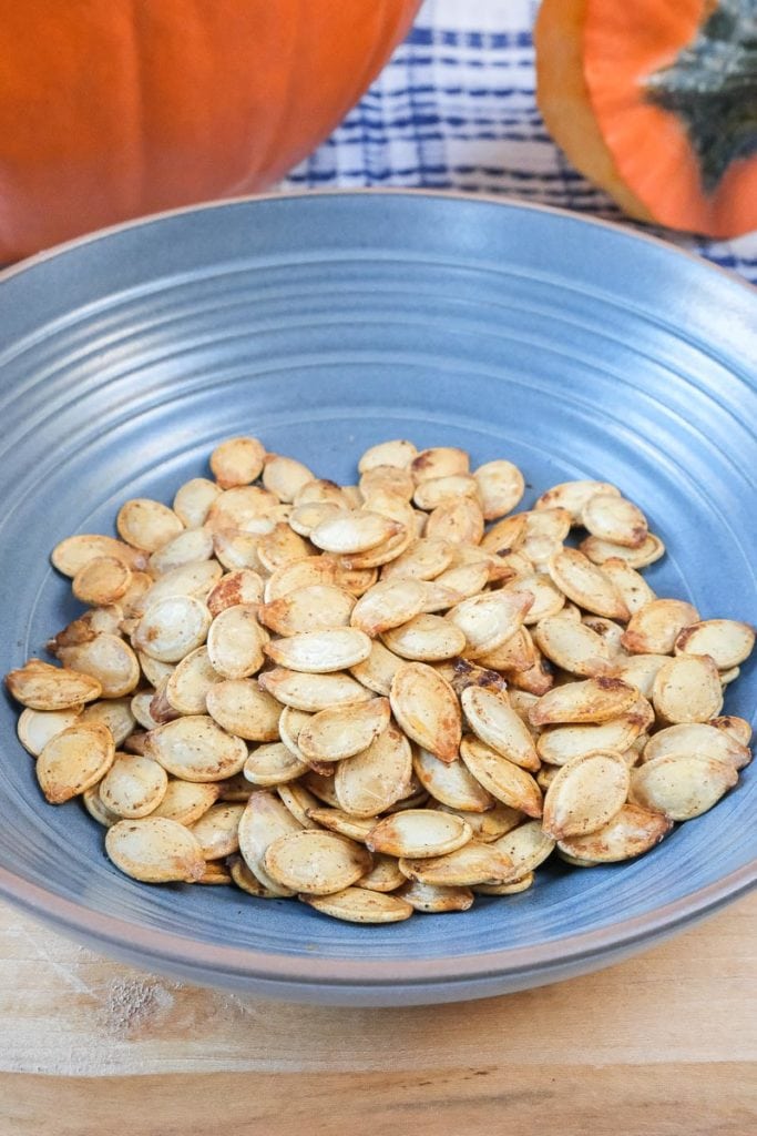 roasted pumpkin seeds in blue bowl on wooden board with pumpkins behind