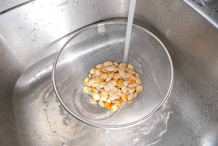 rinsing pumpkin seeds in metal strainer in metallic sink