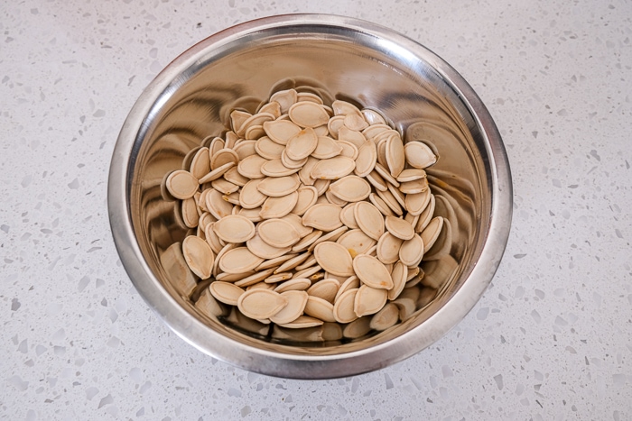 pumpkin seeds in small metallic bowl on white counter