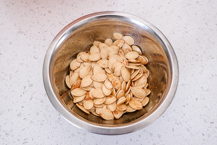 pumpkin seeds with spices in small silver bowl on white counter