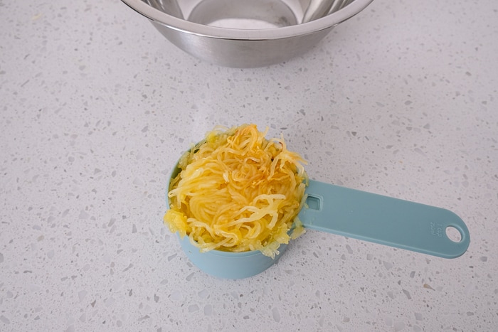 small measuring cup of spaghetti squash on white counter