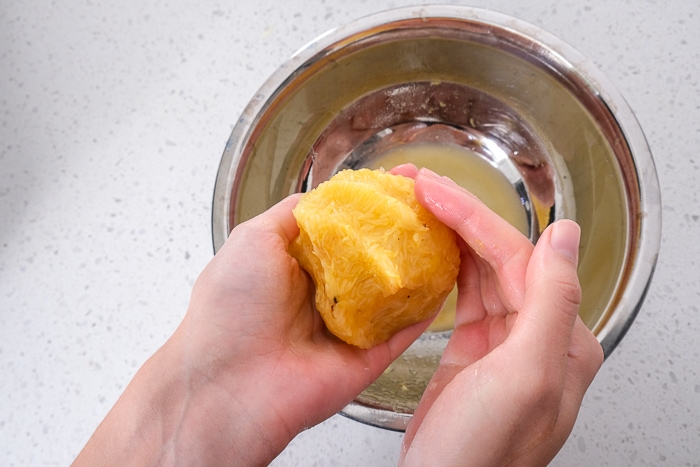 hands holding spaghetti squash over silver mixing bowl on white counter