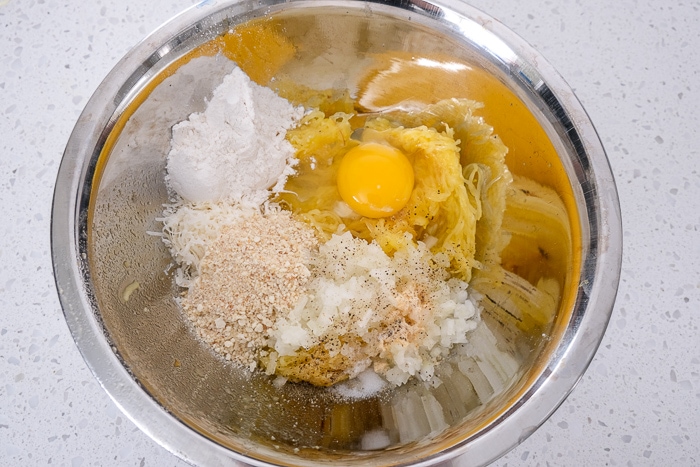silver mixing bowl full of ingredients to make spaghetti squash fritters like egg and flour