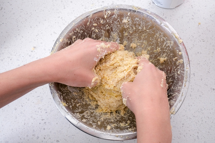 hands mixing fritter batter in silver mixing bowl on counter