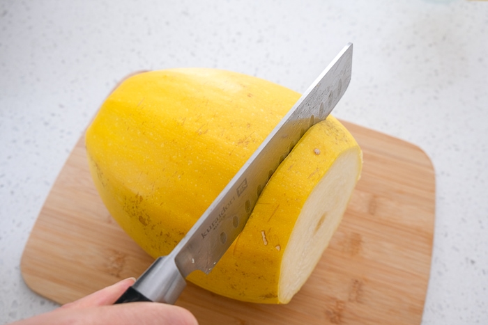 large knife cutting into yellow spaghetti squash on wooden board