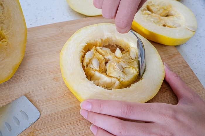 silver spoon removing seeds from inside a spaghetti squash ring on wooden board