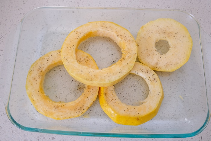 yellow spaghetti squash rings in clear glass dish with oil and spices on top