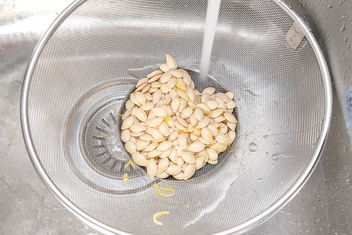 spaghetti squash seeds in metal strainer with water running in metallic sink
