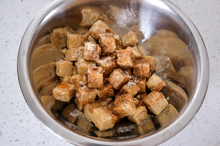 pieces of tempeh in silver mixing bowl with spices and marinade
