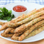 breaded asparagus fries on white plate with ketchup and parsley behind