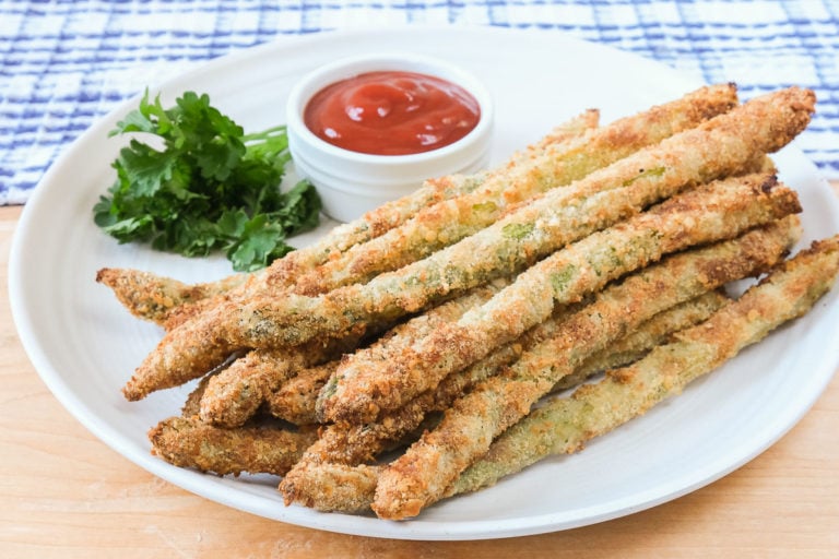 breaded asparagus fries on white plate with ketchup and parsley behind